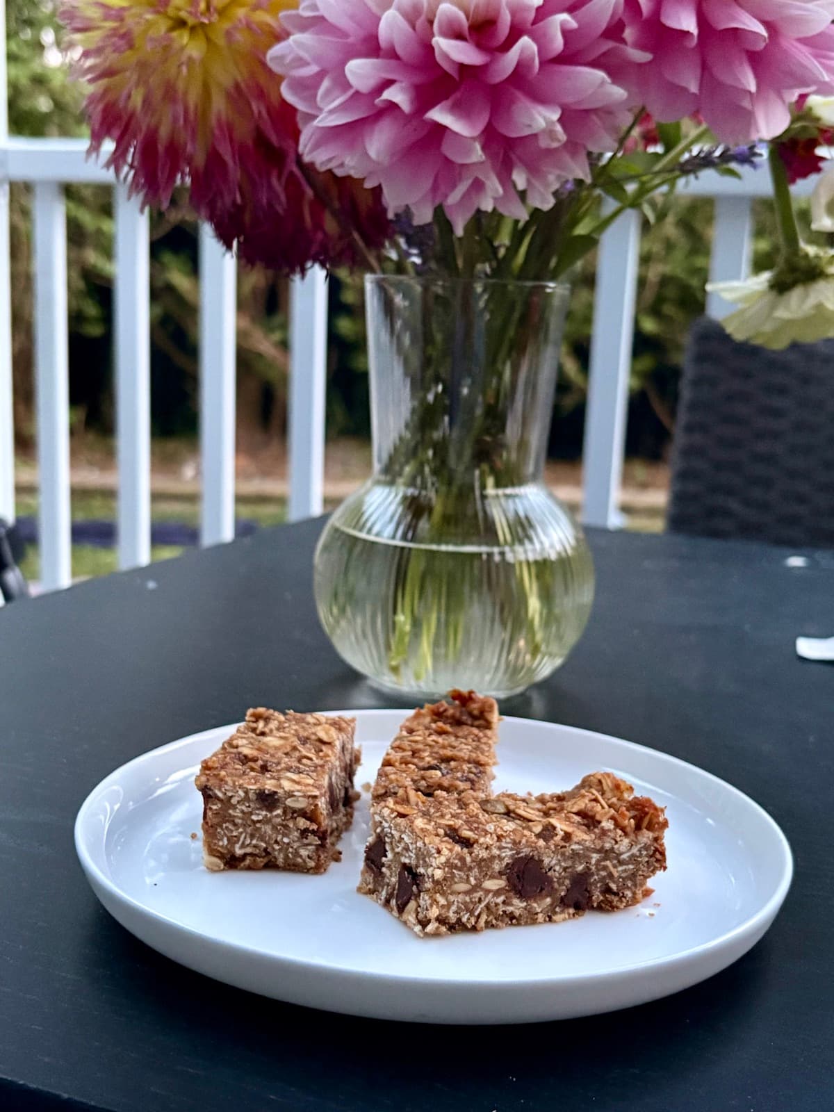 Banana peanut butter granola bars on a white plate with garden dahlias